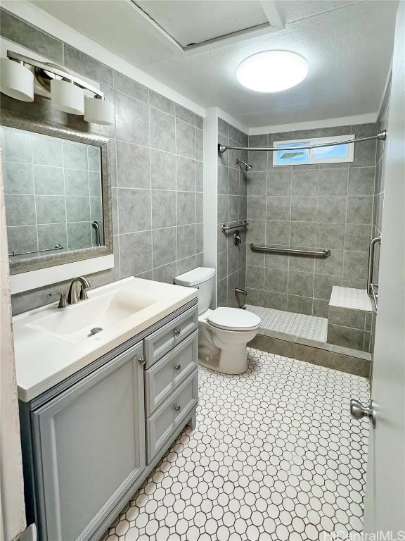 bathroom featuring vanity, toilet, tile walls, and a tile shower