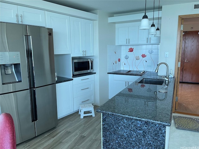 kitchen with white cabinets, a sink, light wood-style flooring, stainless steel appliances, and backsplash