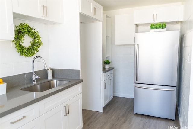 kitchen with white cabinets, stainless steel refrigerator, dark stone countertops, light hardwood / wood-style floors, and sink