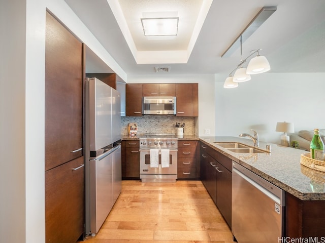 kitchen with sink, light wood-type flooring, kitchen peninsula, stainless steel appliances, and pendant lighting