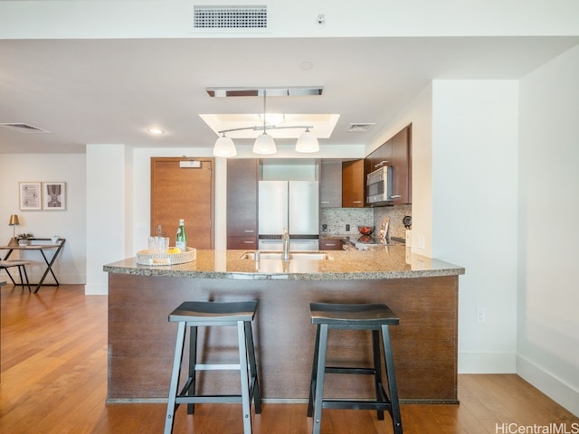 kitchen featuring a kitchen bar, appliances with stainless steel finishes, kitchen peninsula, and light hardwood / wood-style flooring