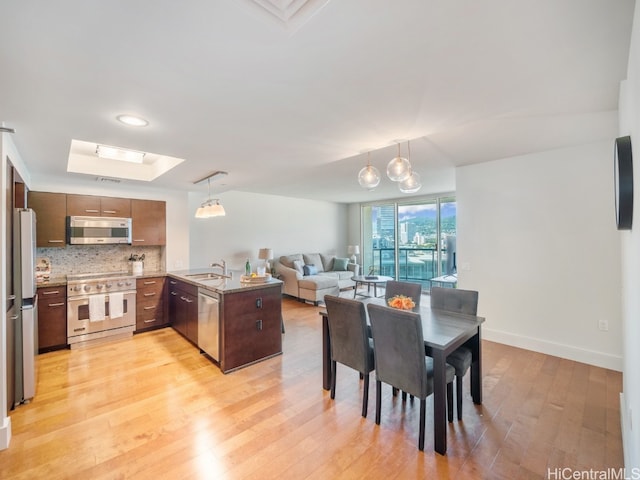 kitchen featuring kitchen peninsula, appliances with stainless steel finishes, sink, light hardwood / wood-style floors, and decorative light fixtures