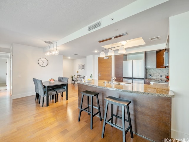 kitchen featuring sink, a breakfast bar, decorative light fixtures, white fridge, and light stone counters