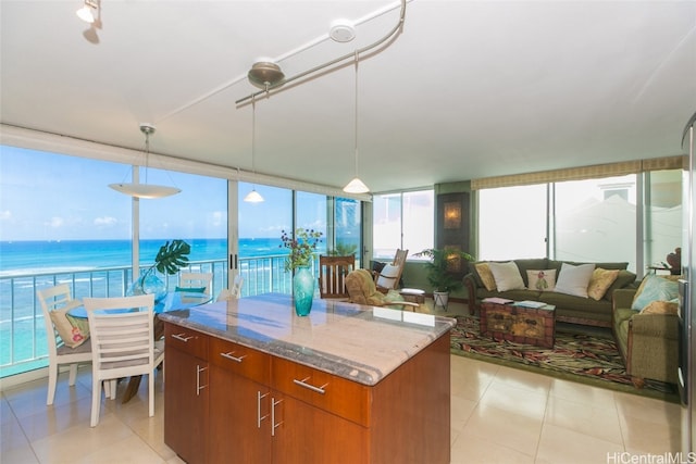 kitchen with hanging light fixtures, light tile patterned floors, a center island, light stone counters, and a water view