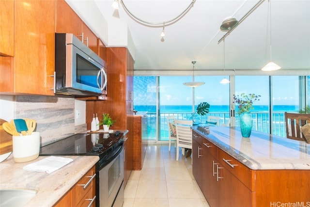 kitchen with tasteful backsplash, appliances with stainless steel finishes, decorative light fixtures, a water view, and light stone counters