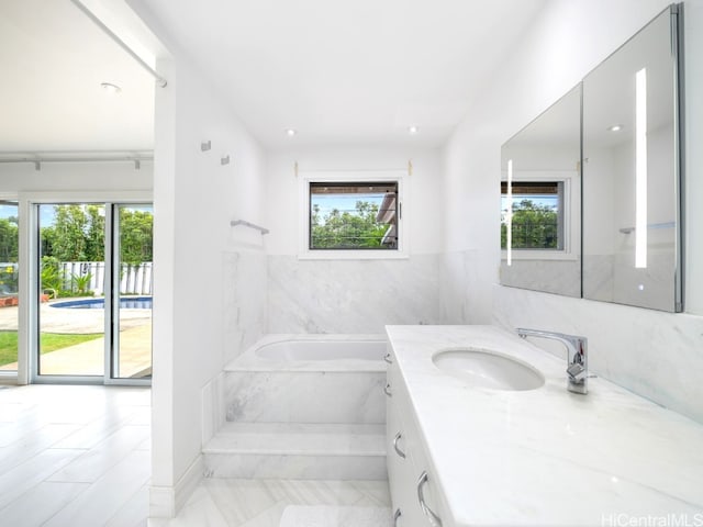 bathroom featuring vanity, a relaxing tiled tub, and plenty of natural light