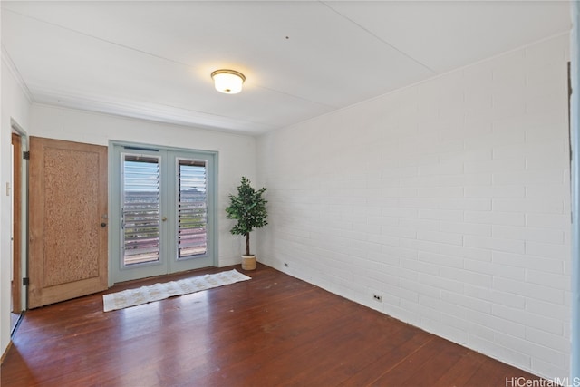 empty room featuring french doors, brick wall, and dark hardwood / wood-style floors