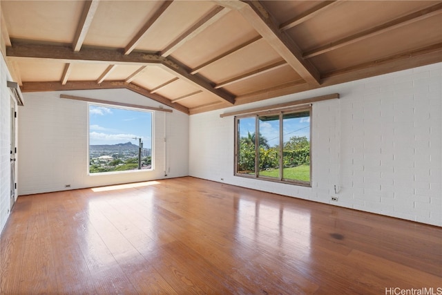 unfurnished room with a mountain view, vaulted ceiling with beams, brick wall, and hardwood / wood-style flooring