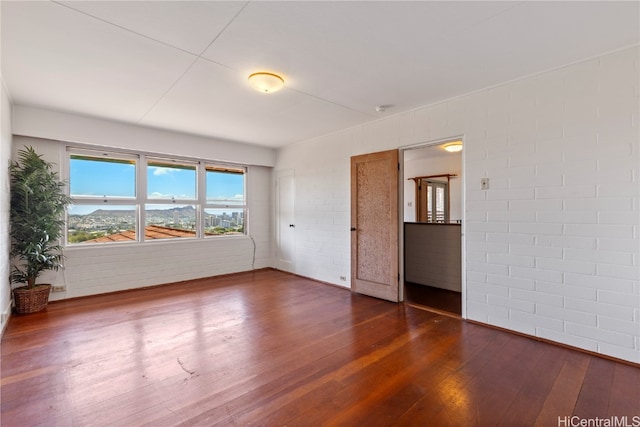 unfurnished room with dark hardwood / wood-style floors and brick wall