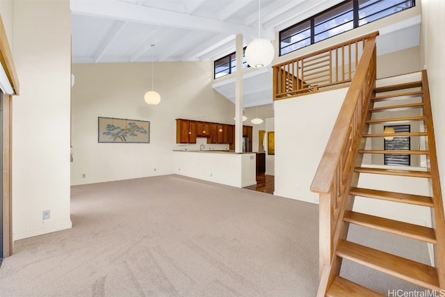 unfurnished living room with a high ceiling, light carpet, and beam ceiling