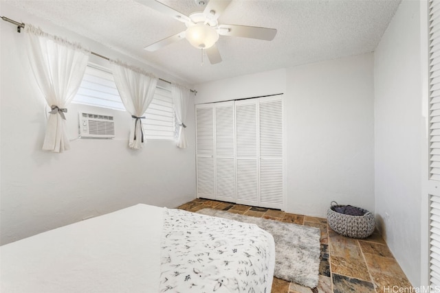 bedroom featuring an AC wall unit, a textured ceiling, a closet, and ceiling fan