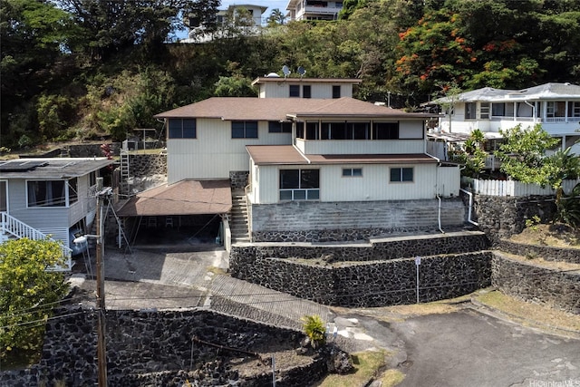 back of house featuring roof with shingles, driveway, and stairway