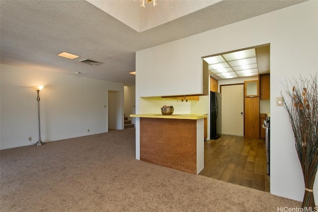 kitchen with kitchen peninsula, dark carpet, a textured ceiling, and black fridge