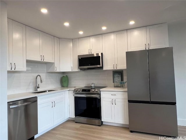 kitchen with white cabinets, sink, decorative backsplash, light hardwood / wood-style floors, and stainless steel appliances