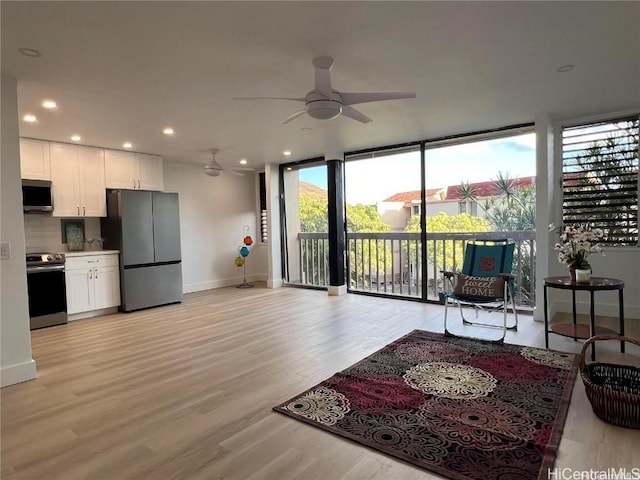 living room featuring ceiling fan, expansive windows, and light wood-type flooring