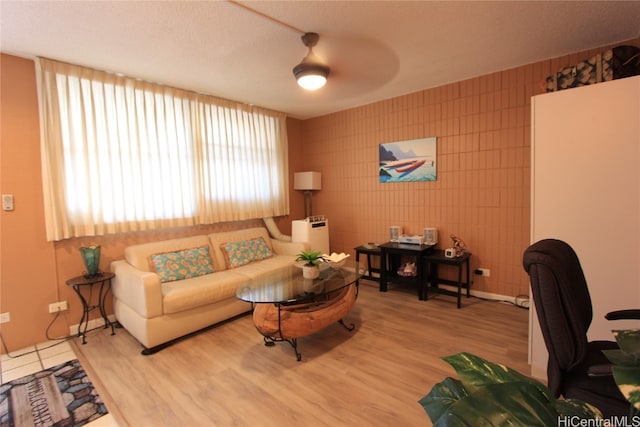 living room with tile walls, hardwood / wood-style flooring, and ceiling fan