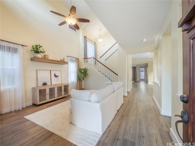 living room featuring light hardwood / wood-style floors, ceiling fan, and a high ceiling