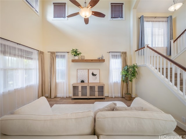 living room featuring light wood-type flooring, ceiling fan, and a towering ceiling