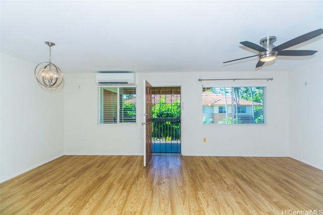 spare room featuring a wall unit AC, light hardwood / wood-style flooring, and ceiling fan with notable chandelier