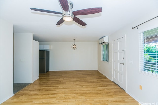 interior space with ceiling fan, an AC wall unit, and light hardwood / wood-style flooring