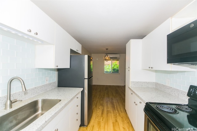 kitchen featuring white cabinets, hanging light fixtures, light hardwood / wood-style flooring, black appliances, and sink