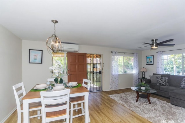 dining area featuring light wood-type flooring, an AC wall unit, and ceiling fan with notable chandelier