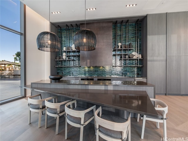 bar with tasteful backsplash, sink, light wood-type flooring, and pendant lighting