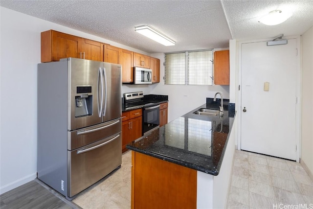 kitchen with a textured ceiling, stainless steel appliances, dark stone counters, and sink