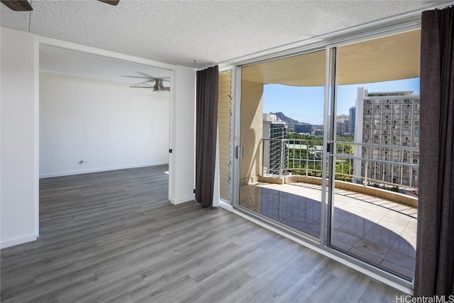 empty room with ceiling fan, expansive windows, a textured ceiling, and hardwood / wood-style flooring