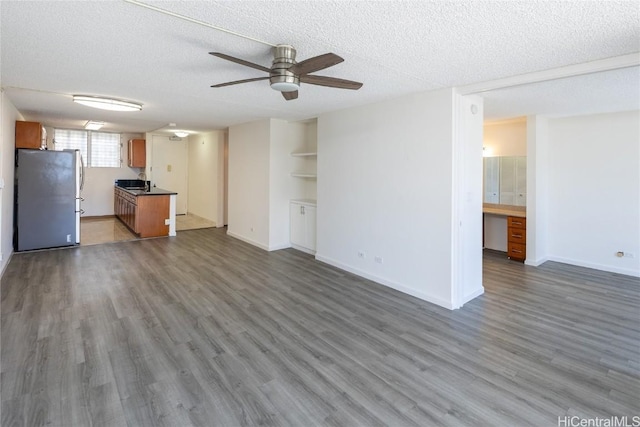 unfurnished living room featuring built in shelves, a textured ceiling, ceiling fan, dark wood-type flooring, and sink