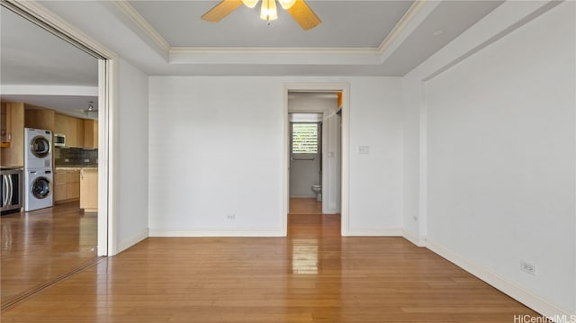 empty room featuring a raised ceiling, ornamental molding, light wood-type flooring, and stacked washer and clothes dryer