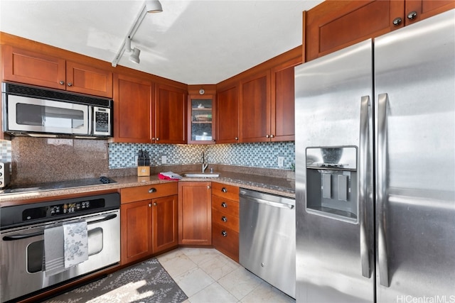 kitchen with decorative backsplash, track lighting, dark stone countertops, sink, and stainless steel appliances