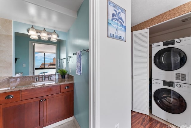 clothes washing area with stacked washer / drying machine, sink, and hardwood / wood-style flooring