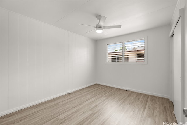 spare room featuring light hardwood / wood-style flooring, wooden walls, and ceiling fan