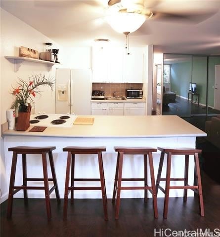 kitchen with a breakfast bar area, decorative backsplash, white cabinets, and white appliances