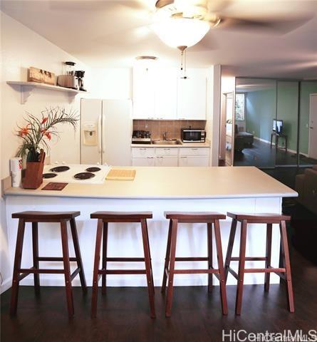 kitchen with white appliances, decorative backsplash, white cabinets, a peninsula, and light countertops