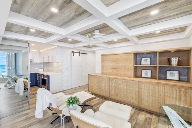 sitting room with beam ceiling, coffered ceiling, a barn door, and light hardwood / wood-style floors