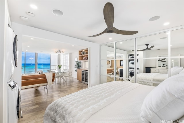 bedroom featuring stacked washer / drying machine, recessed lighting, a water view, ceiling fan, and wood finished floors