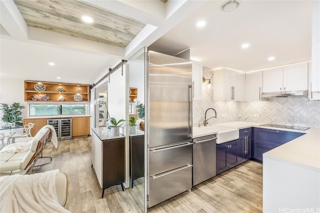 kitchen with a barn door, blue cabinets, white cabinetry, light countertops, and appliances with stainless steel finishes