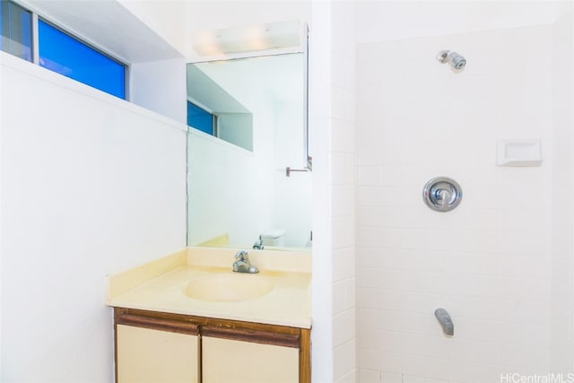 bathroom featuring vanity, a tile shower, and toilet