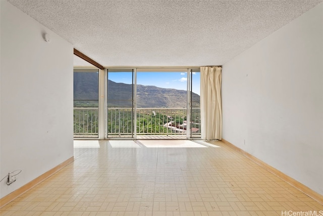 unfurnished room with a mountain view, a textured ceiling, and floor to ceiling windows