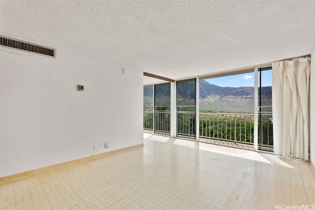 unfurnished room featuring a mountain view, a textured ceiling, and floor to ceiling windows