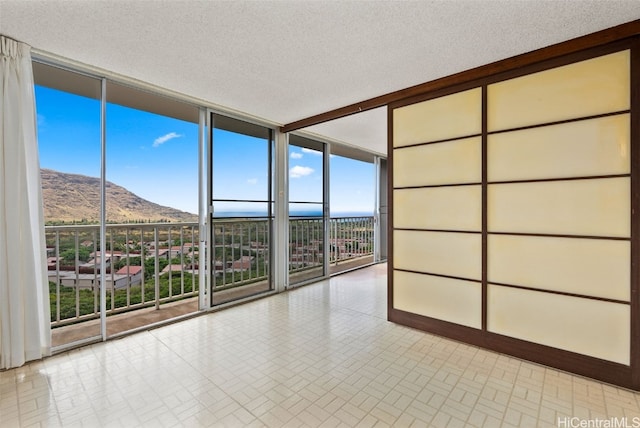 unfurnished room featuring a wall of windows, a mountain view, and a textured ceiling