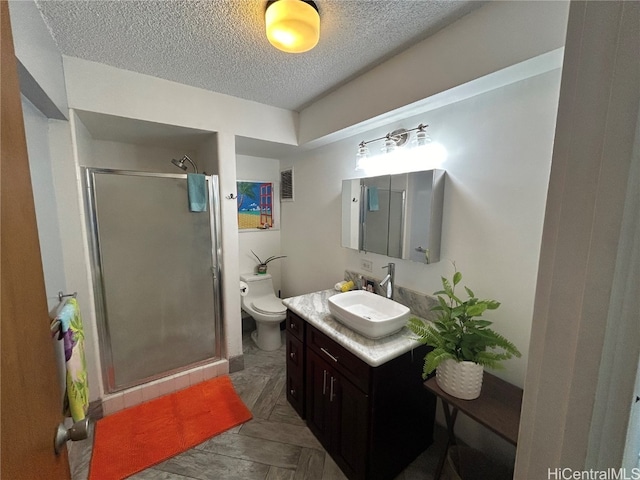 bathroom with vanity, a textured ceiling, toilet, and a shower with door