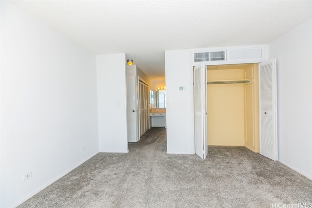 unfurnished bedroom featuring a textured ceiling, light colored carpet, and ensuite bathroom