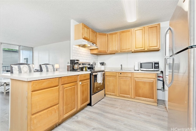 kitchen with sink, a textured ceiling, kitchen peninsula, light hardwood / wood-style floors, and stainless steel appliances