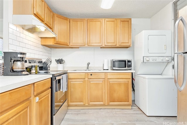 kitchen with stacked washing maching and dryer, light hardwood / wood-style flooring, stainless steel appliances, sink, and a textured ceiling