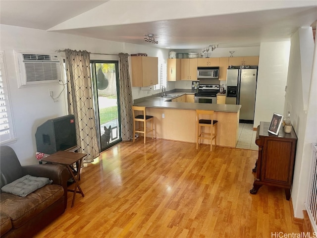 kitchen featuring an AC wall unit, kitchen peninsula, stainless steel appliances, sink, and light wood-type flooring