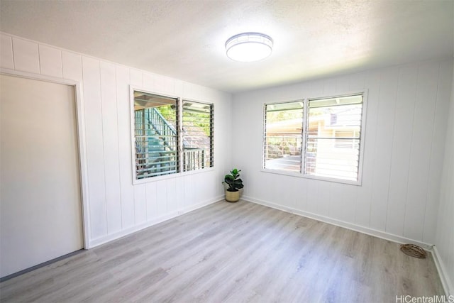 empty room with a textured ceiling and light hardwood / wood-style flooring