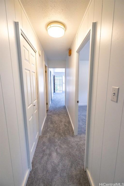 hallway featuring dark carpet and a textured ceiling